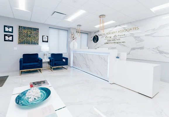 An angled view of the reception desk at Plastic Surgery Associates, showing the marble-patterned wall behind the counter and modern gold lighting fixtures.