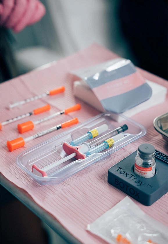 Close-up of medical supplies including syringes, needles, and a Botox vial on a pink sterile tray.