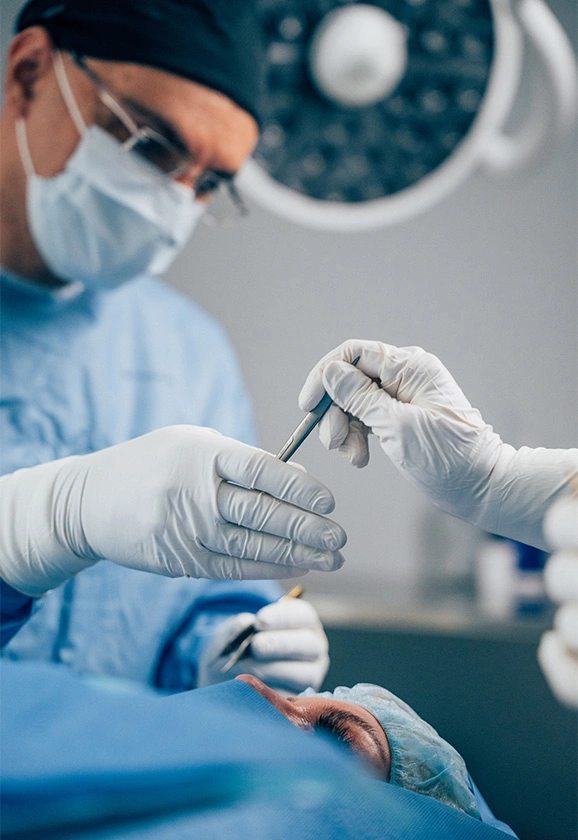 Close-up of Dr. Papafragkou's gloved hands passing a surgical instrument over a patient during surgery.