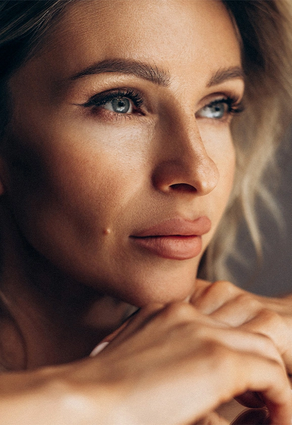 A close-up profile of a woman with blonde hair and defined makeup looking off into the distance.